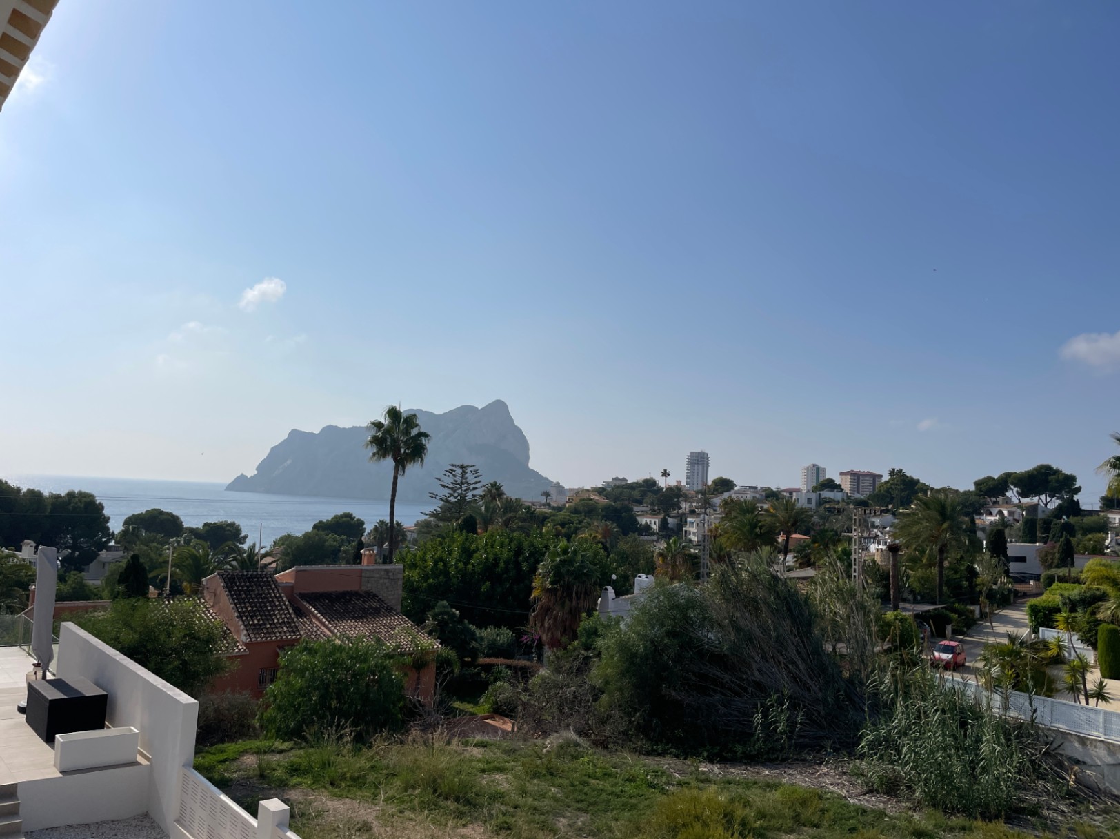 Panoramic views of the Peñón de Ifach and the Mediterranean Sea from an elevated terrace position in Bassetes, Calpe, framed by lush greenery.