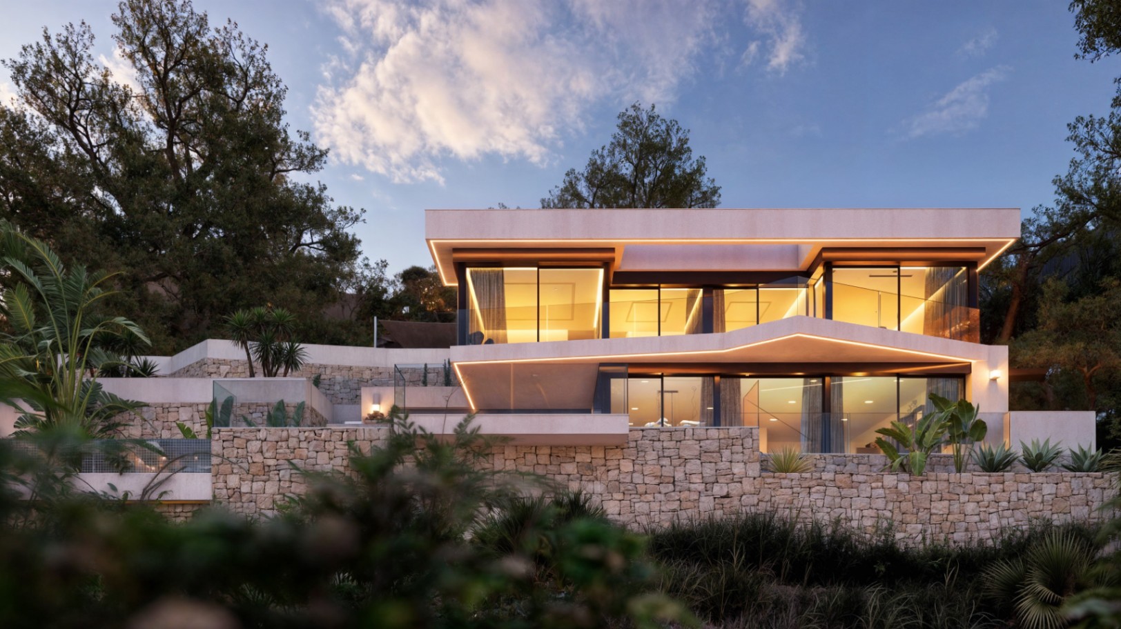 Modern two-level facade featuring natural stone walls, integrated LED lighting under cantilevered roofs, and floor-to-ceiling windows showcasing warm interiors.