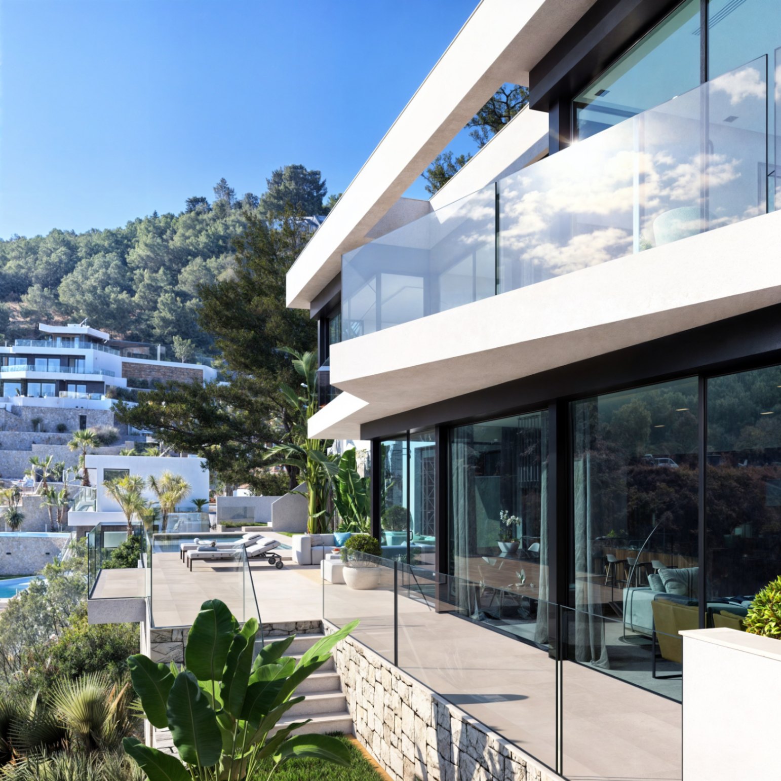 Modern two-story facade featuring floor-to-ceiling glass doors, transparent railings, and stone-walled terraces surrounded by lush Mediterranean greenery.