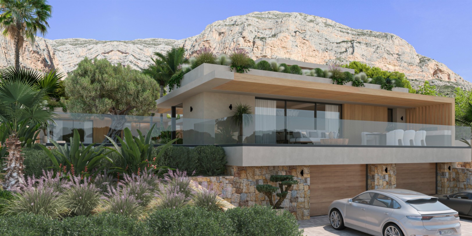 Modern villa exterior featuring natural stone walls, large glass sliders, and a glass-railed terrace, set against the backdrop of the Montgó mountain in Jávea.