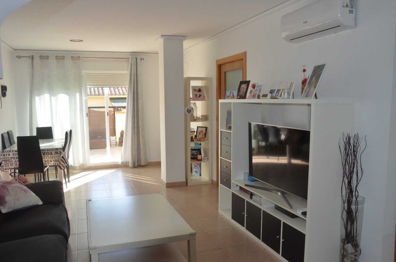 Bright living and dining area featuring ceramic tile flooring, a modular TV unit, wall-mounted air conditioning, and direct access to an outdoor patio.