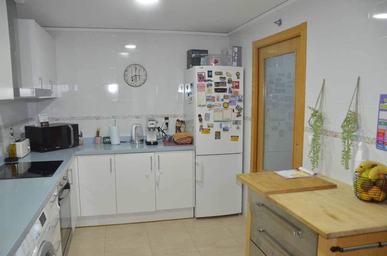 Functional kitchen featuring white cabinetry, a light blue countertop, and integrated appliances. Includes a wooden prep island and tiled walls with a decorative border.