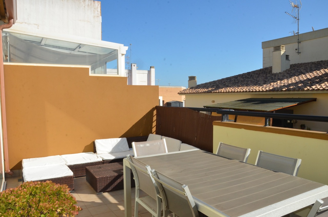 Rooftop terrace featuring a grey dining set and a wicker lounge area with white cushions, set against ochre walls under a clear sky.