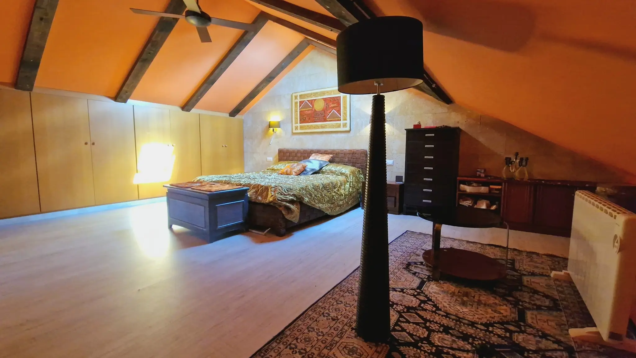 Attic bedroom featuring exposed dark wood beams, integrated light-wood wardrobes, and a natural stone accent wall under the sloped ceiling.