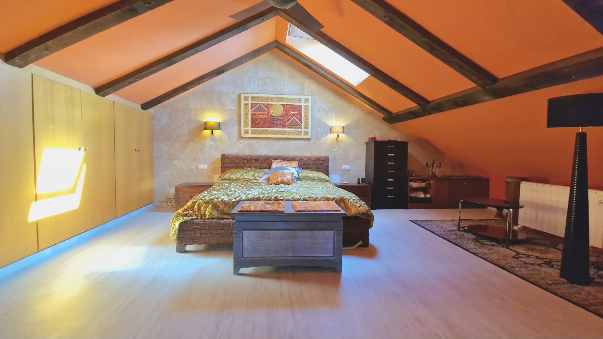 Attic bedroom featuring exposed dark wood beams, orange vaulted ceilings, a stone accent wall, and integrated light wood wardrobes.
