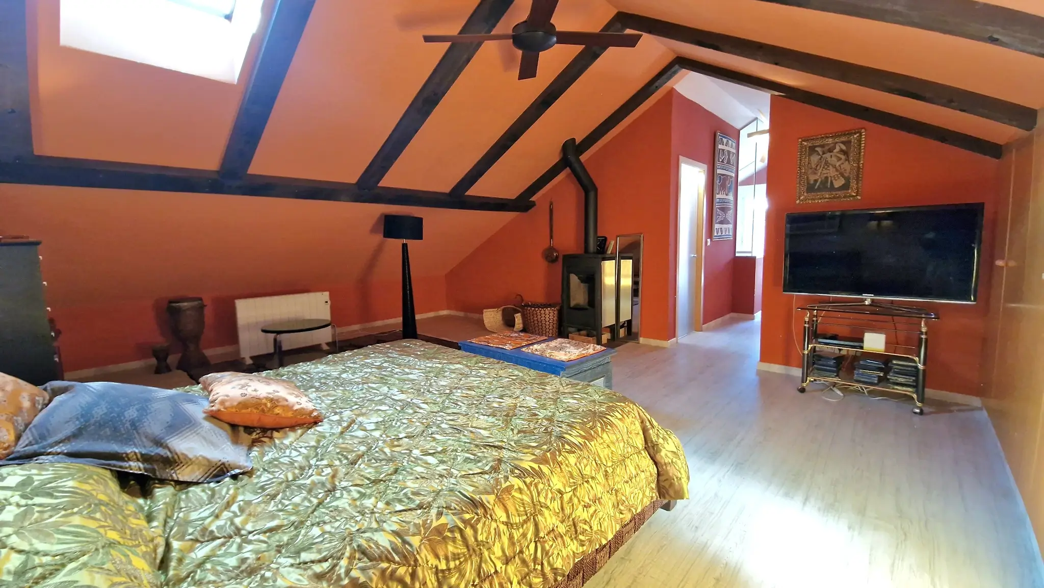 Attic bedroom featuring exposed dark wood beams, terracotta walls, a wood-burning stove, and a skylight providing natural light.