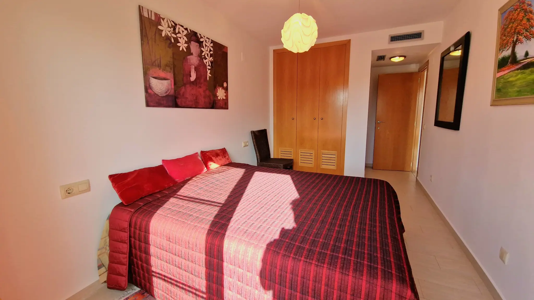 Bedroom featuring a double bed with maroon striped bedding, built-in wooden wardrobes, and oriental-inspired wall art above the headboard.