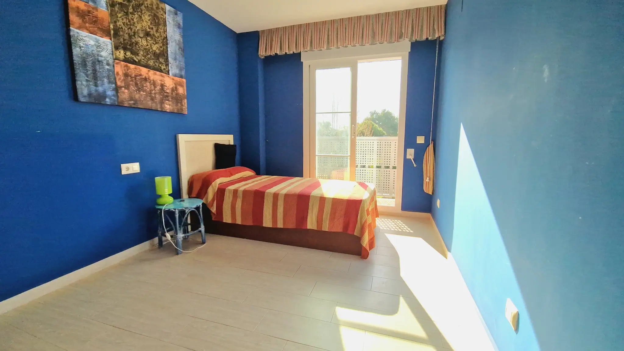 Bedroom featuring deep blue walls, a single bed with striped bedding, and direct access to a balcony through sliding glass doors.