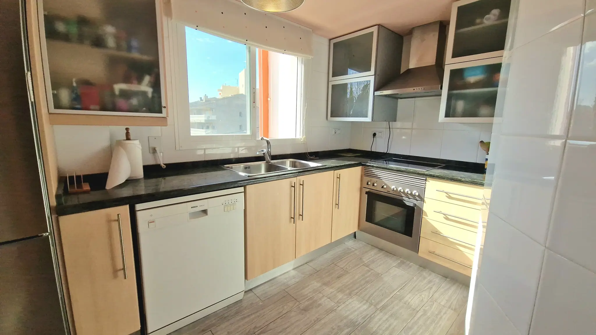 Functional kitchen featuring dark granite countertops, light wood cabinetry, and integrated appliances. It includes a Bosch dishwasher and a window providing natural light.