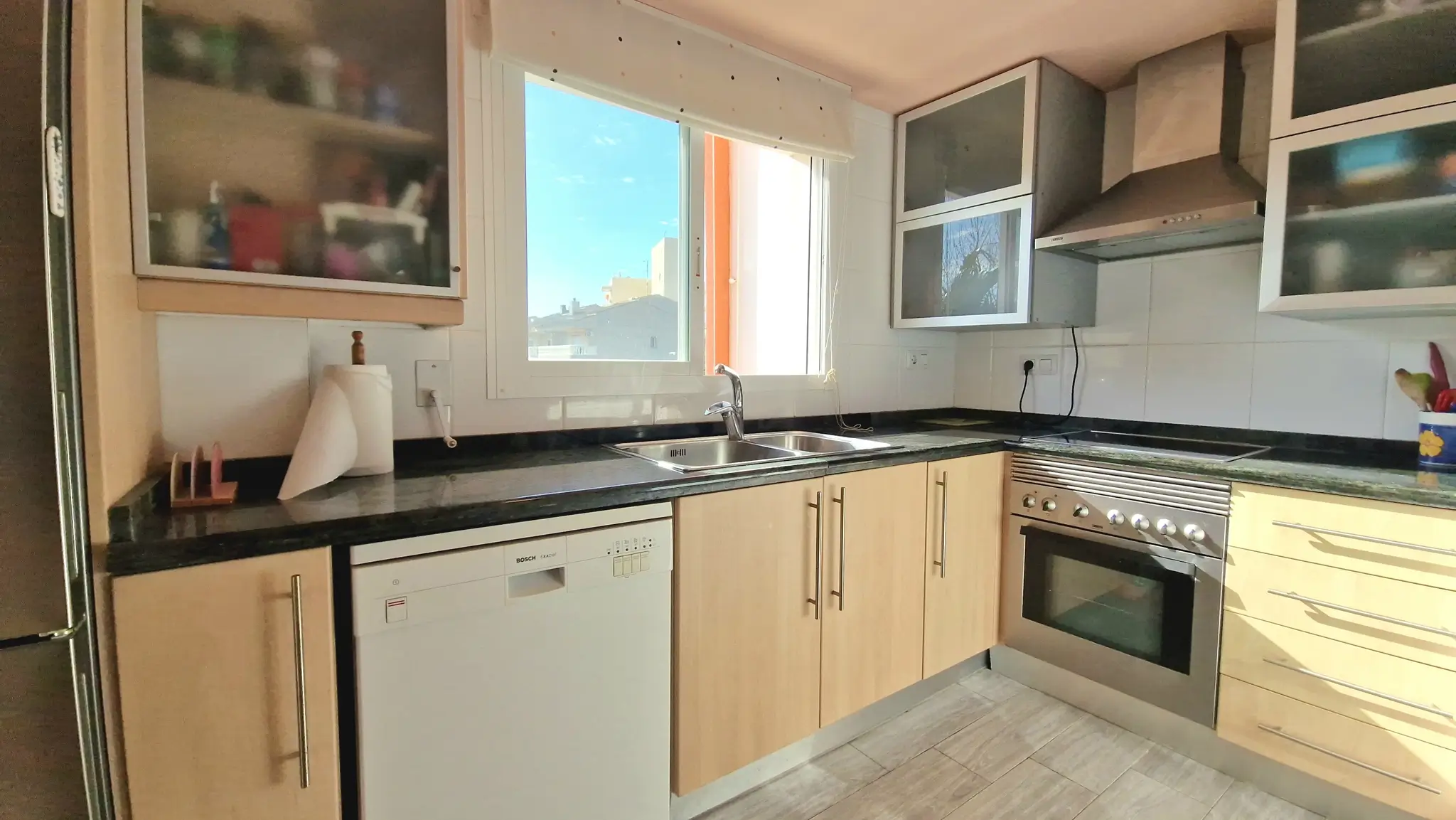 Functional kitchen featuring light wood cabinetry, dark granite countertops, and integrated appliances including a Bosch dishwasher and stainless steel oven.