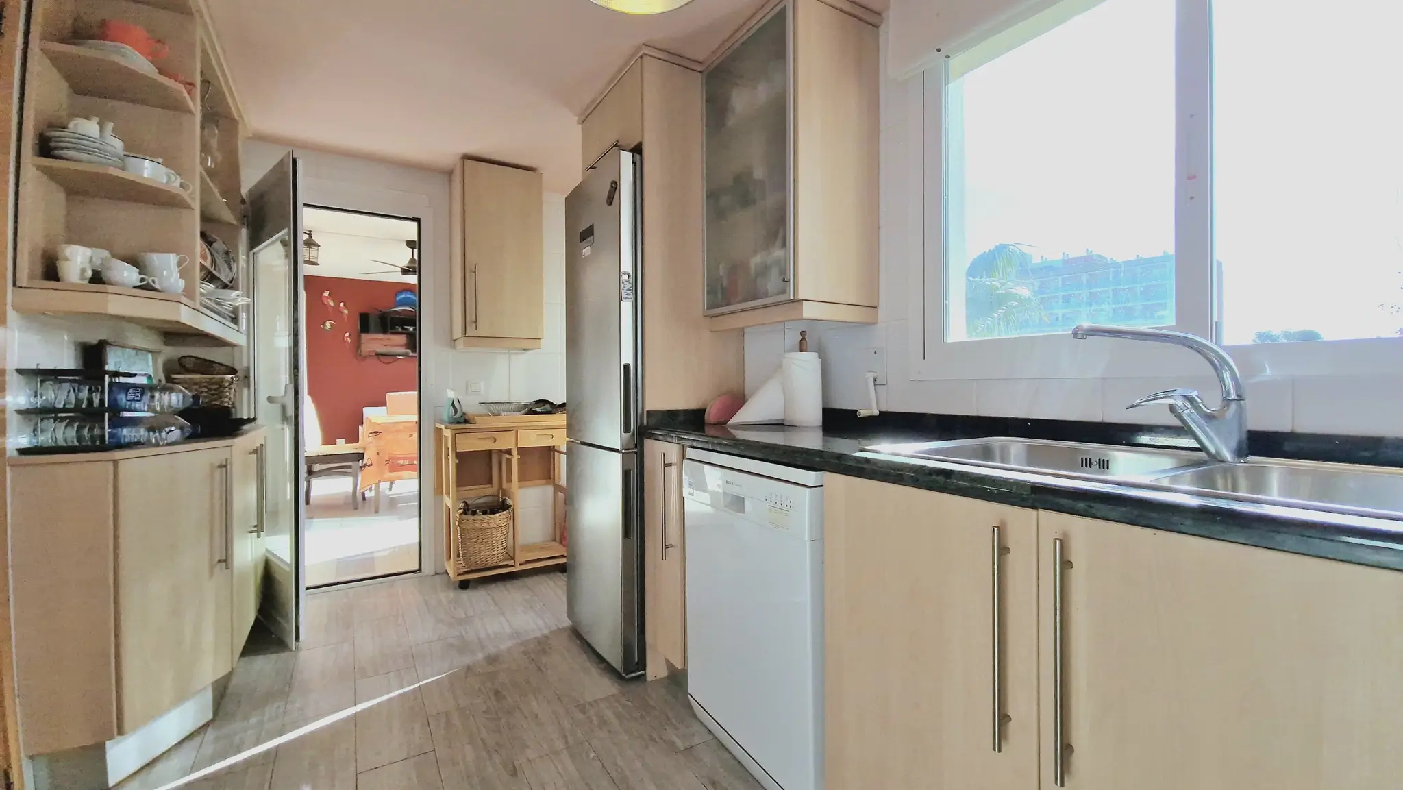 Functional kitchen featuring light wood cabinetry, dark granite countertops, stainless steel appliances, and a large window for natural lighting.