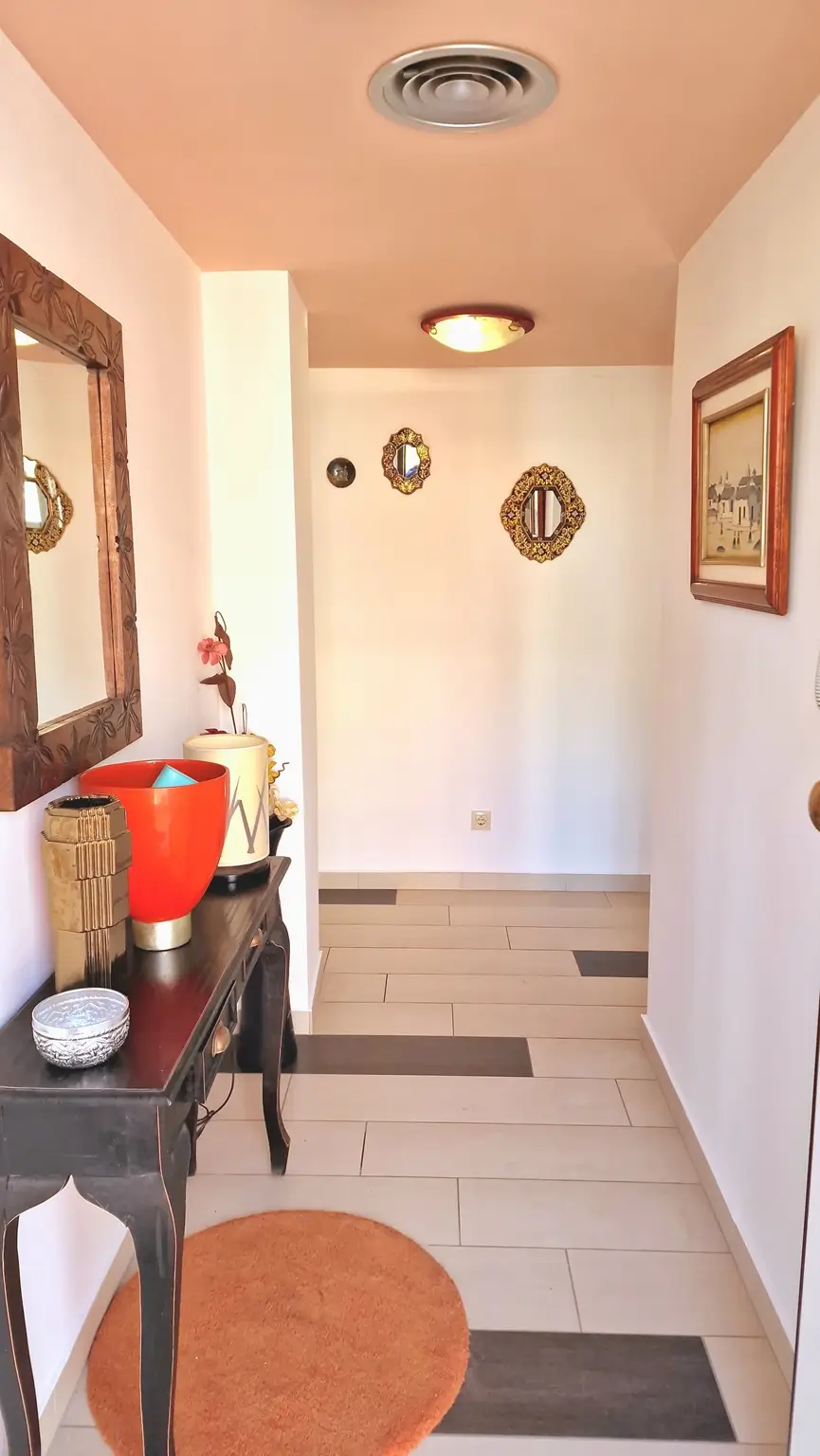 Hallway featuring tiled flooring with dark accents, a dark wood console table, and decorative wall mirrors under a peach-toned ceiling.