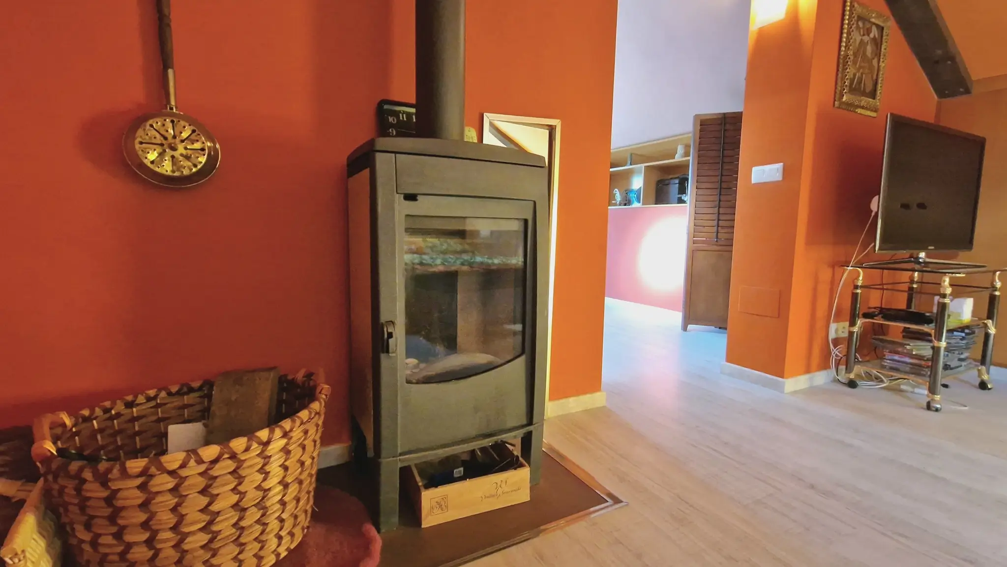 Modern black wood-burning stove positioned against terracotta walls, featuring light wood flooring and a traditional wicker basket for firewood.