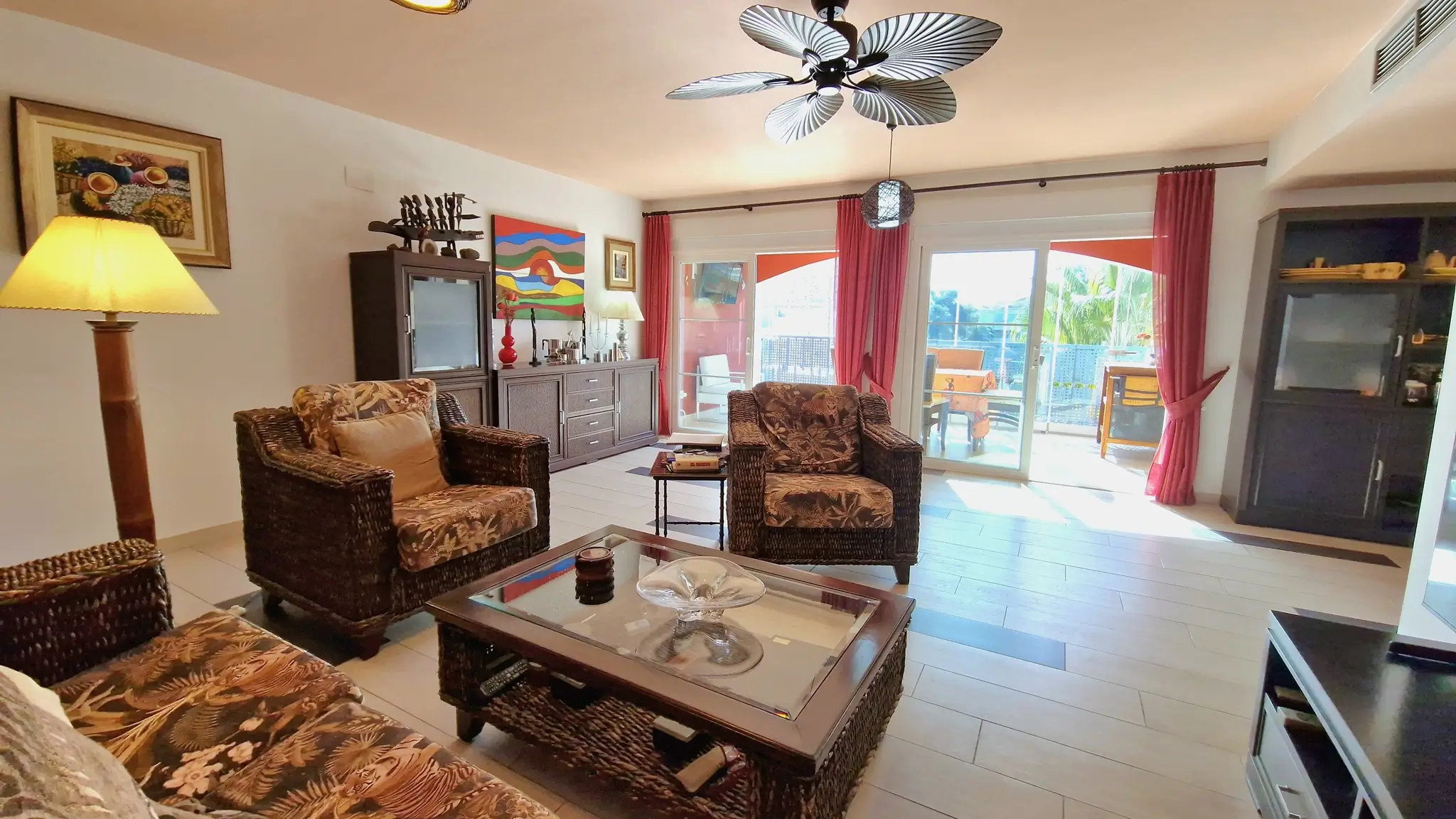 Spacious living room featuring wicker furniture with tropical patterns, a palm-leaf ceiling fan, and direct access to a terrace through sliding glass doors.