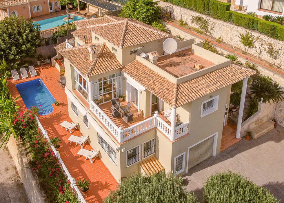 Aerial view of a multi-level villa with terracotta roofing, a private swimming pool, and terraces featuring white balustrades and outdoor dining.