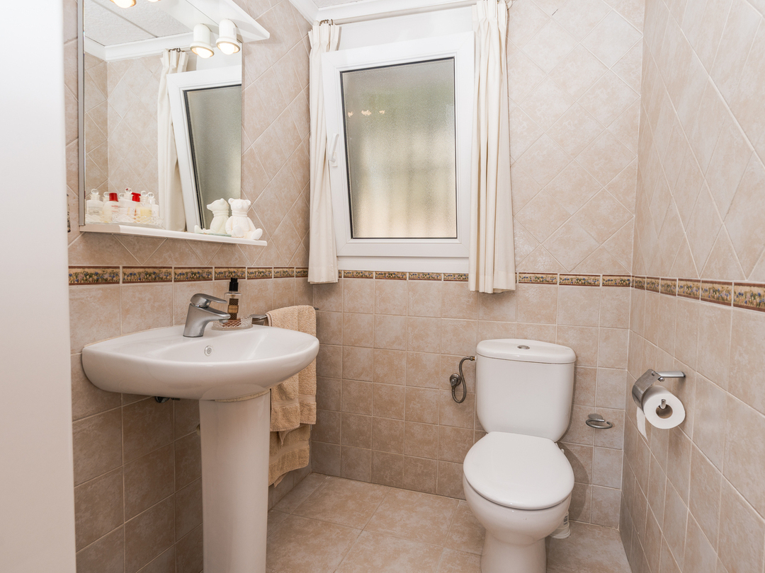 Bathroom featuring a pedestal sink, white ceramic toilet, and beige tiled walls with a decorative border and frosted glass window.