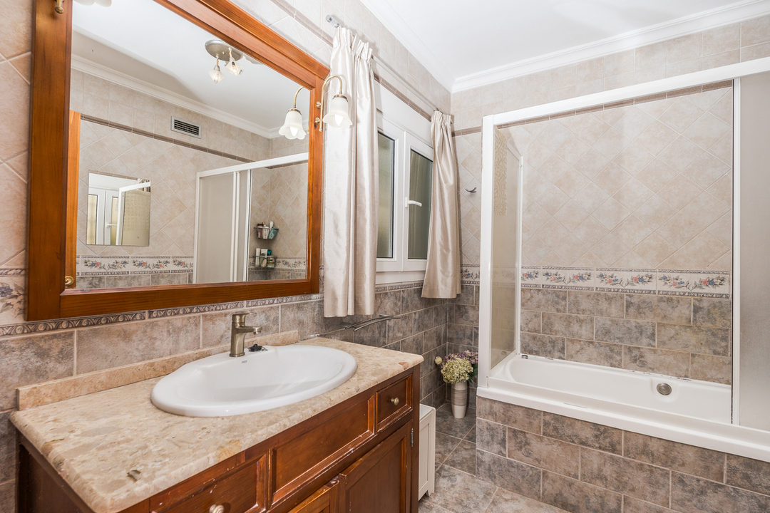 Bathroom featuring a wooden vanity with a marble top, a large framed mirror, and a bathtub with a sliding screen and decorative wall tiling.