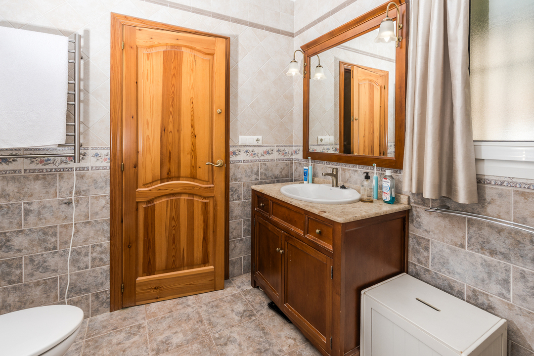 Bathroom featuring a wooden vanity with stone countertop, matching framed mirror, and natural wood door. Walls are finished with decorative ceramic tiles and a floral border.
