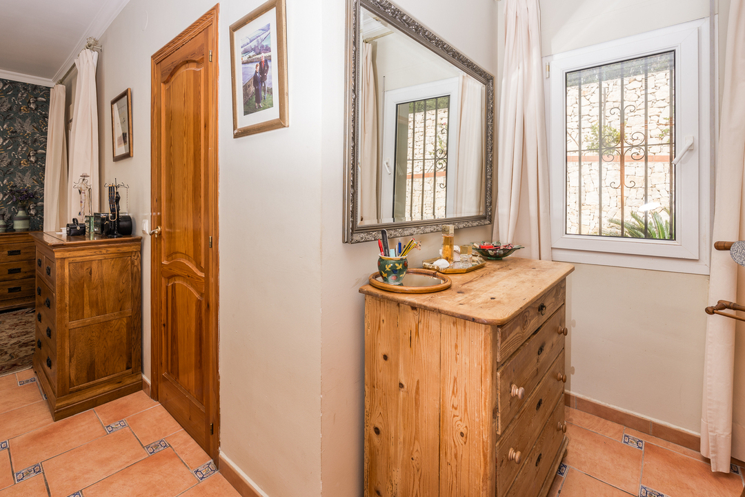 Bedroom corner featuring a pine chest of drawers, terracotta tile flooring with decorative inserts, and a large silver-framed mirror next to a window.