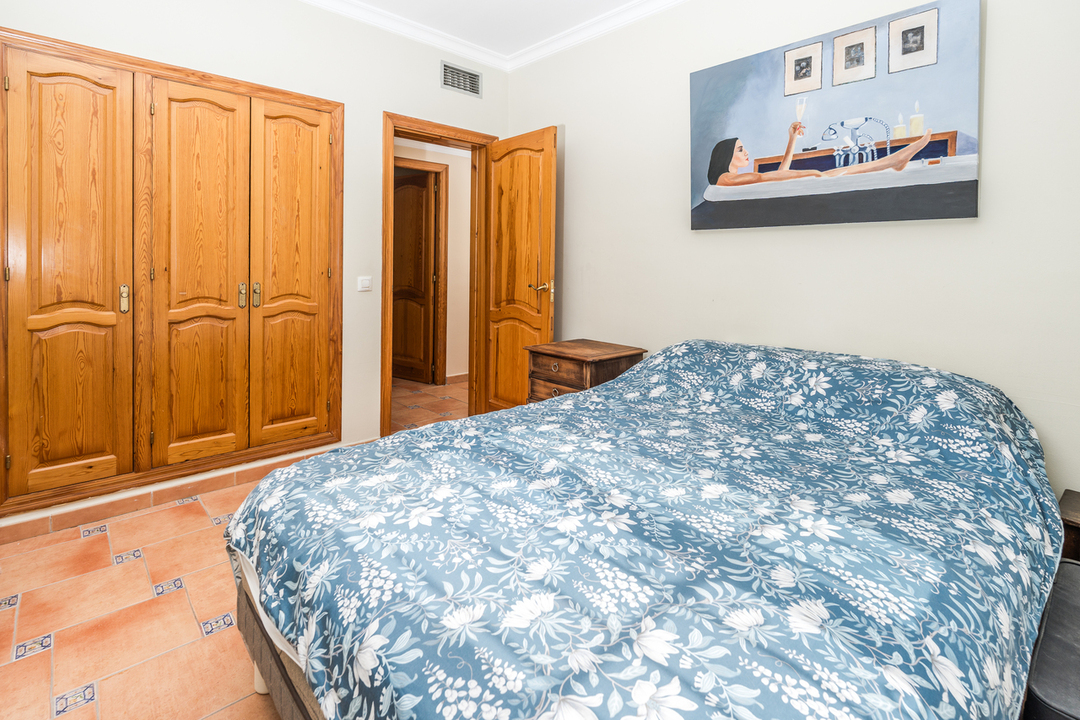 Bedroom featuring a built-in natural wood wardrobe, terracotta tile flooring with blue accents, and a double bed with floral textiles.