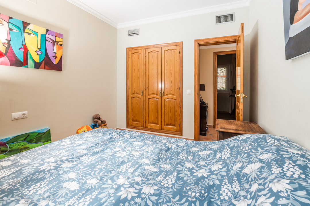 Bedroom featuring a built-in wooden wardrobe, light-colored walls with modern art, and a bed with blue floral patterned linens.