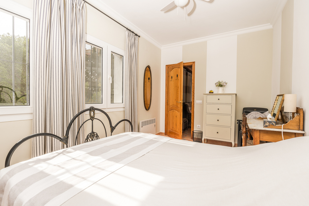 Bedroom featuring a wrought iron headboard, vintage wooden desk, and large windows with striped curtains providing natural light and garden views.