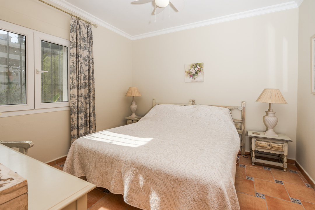 Bedroom featuring terracotta tile flooring with blue accents, distressed wood nightstands, and natural light through a window with toile-style curtains.