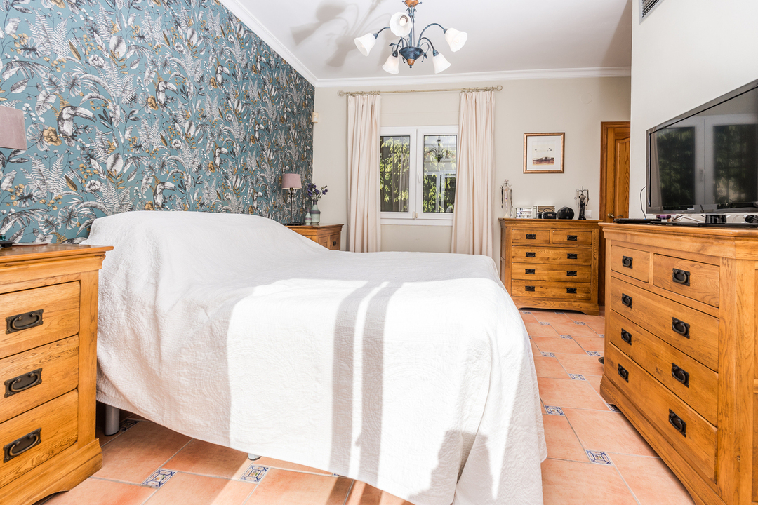 Bedroom featuring tropical-themed wallpaper, matching wooden dressers, and terracotta flooring with blue decorative tile inserts.