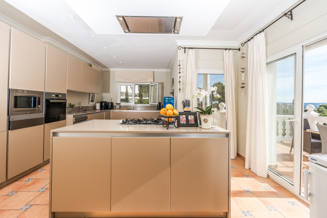 Contemporary kitchen featuring a central island with a gas hob, integrated appliances, and terracotta flooring. Large sliding doors provide direct terrace access.