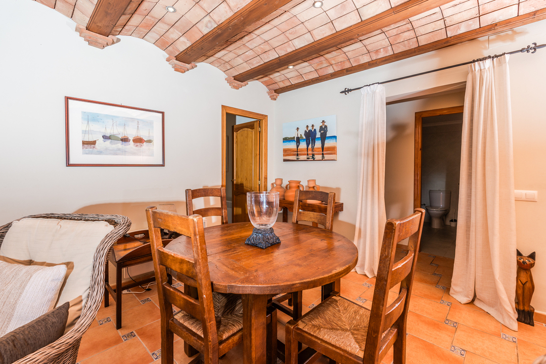 Dining area featuring a vaulted brick ceiling with exposed wooden beams, terracotta tile flooring, and a rustic round wooden table with matching chairs.