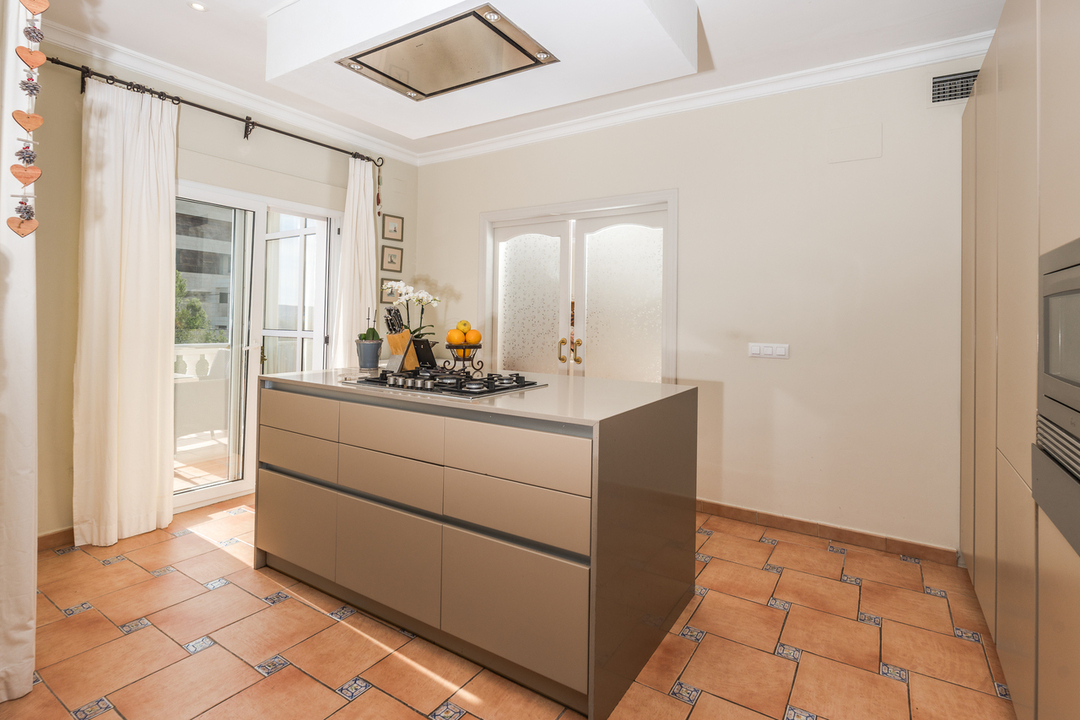 Kitchen featuring a central island with gas cooktop, terracotta tile flooring, and glass door access to the outdoor terrace.