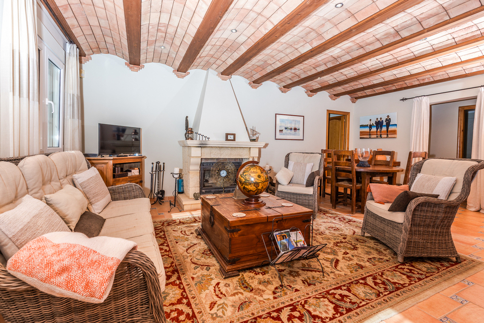 Living area featuring a Catalan vaulted ceiling with wooden beams, a stone fireplace, and rustic wicker furniture over terracotta tile flooring.