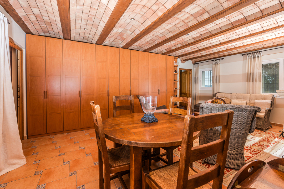 Living area featuring a traditional Catalan vaulted ceiling with wooden beams, terracotta tile flooring, and a large built-in wooden wardrobe wall.