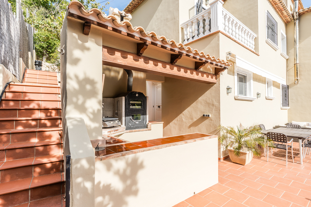 Outdoor kitchen featuring a built-in wood-fired oven, terracotta tiled counters, and a shaded prep area next to the dining terrace and stairs.
