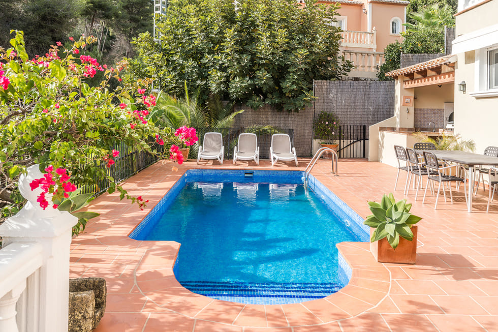 Rectangular swimming pool with blue mosaic tiles, surrounded by a terracotta terrace, sun loungers, and an outdoor dining area framed by bougainvillea.