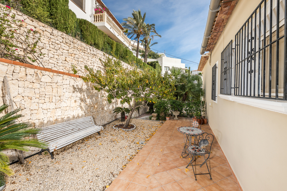 Side patio featuring terracotta tiling, a gravel garden with a white bench, and a natural stone retaining wall.