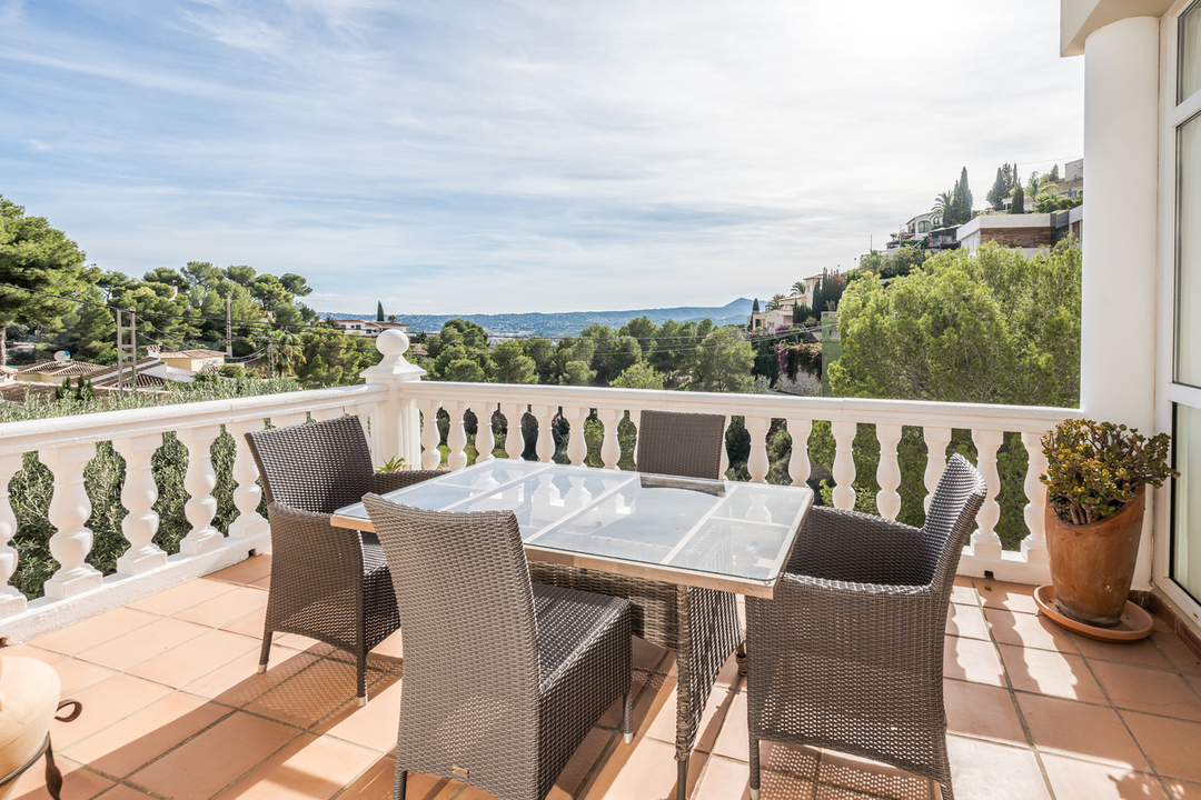 Terrace with terracotta tiling and white balustrade, featuring a wicker dining set with panoramic views of the valley and distant mountains.