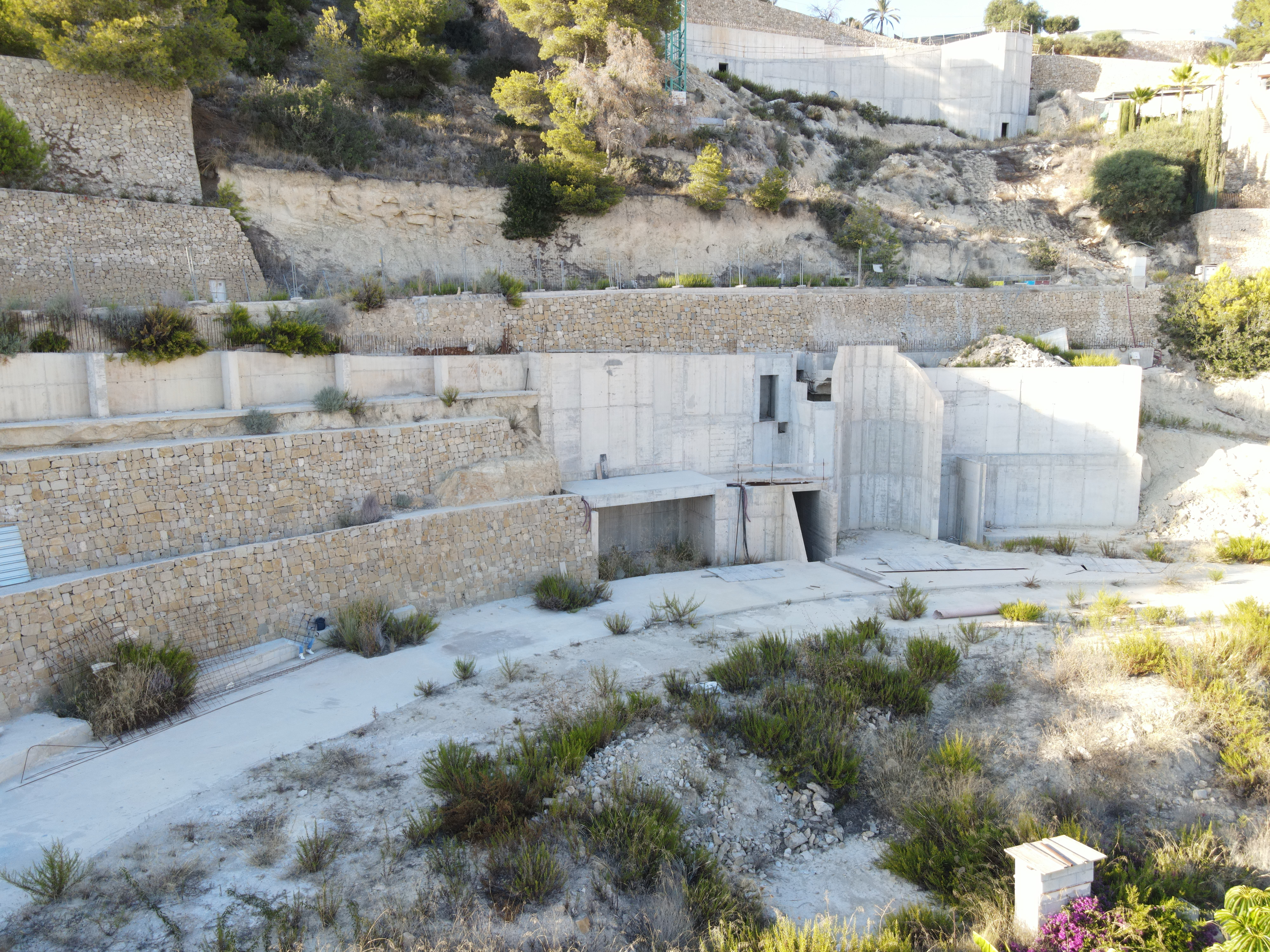 Construction site view showing tiered dry stone retaining walls and reinforced concrete structures integrated into the hillside.