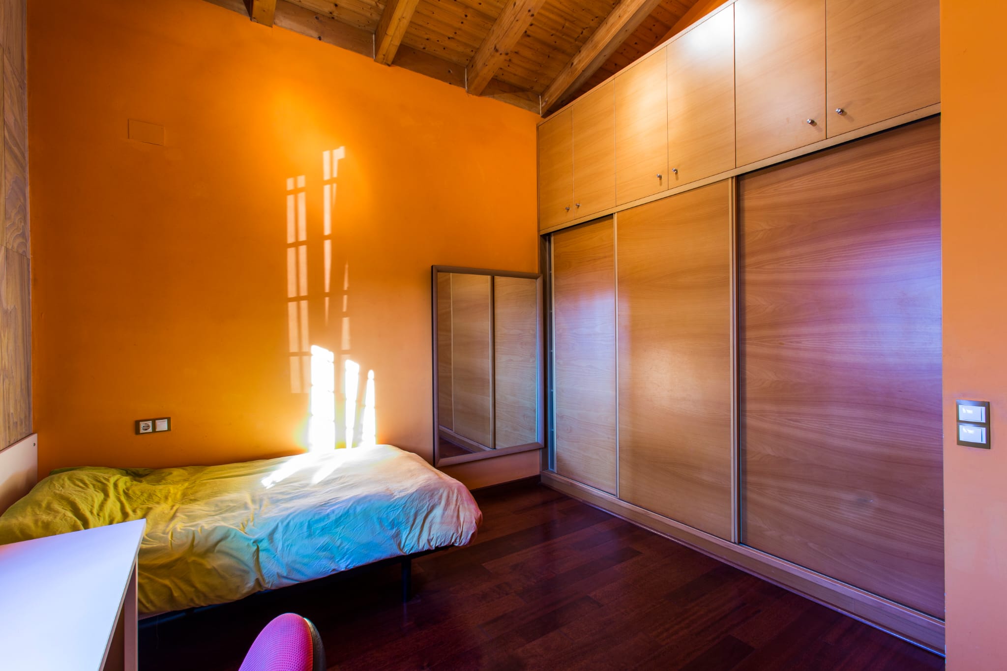Bedroom featuring orange walls, exposed wooden beam ceilings, and a large built-in wooden wardrobe with sliding doors.