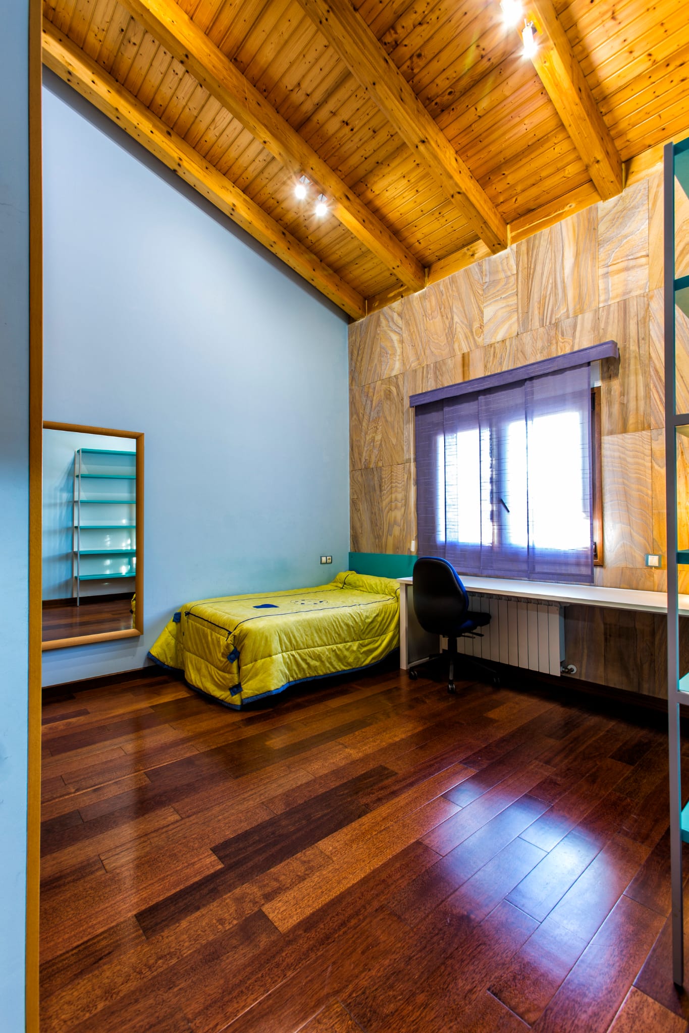Bedroom featuring vaulted wooden beam ceilings, dark hardwood floors, an integrated study desk, and a distinctive textured stone-effect accent wall.