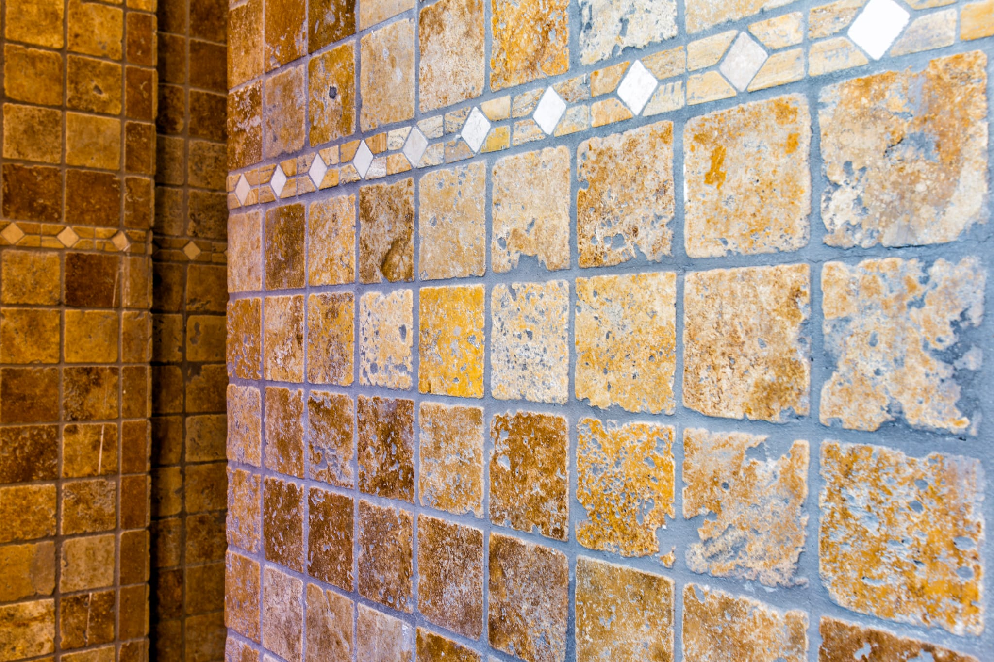 Close-up of rustic ochre stone tiles with a textured finish and a decorative diamond-patterned border inlay.