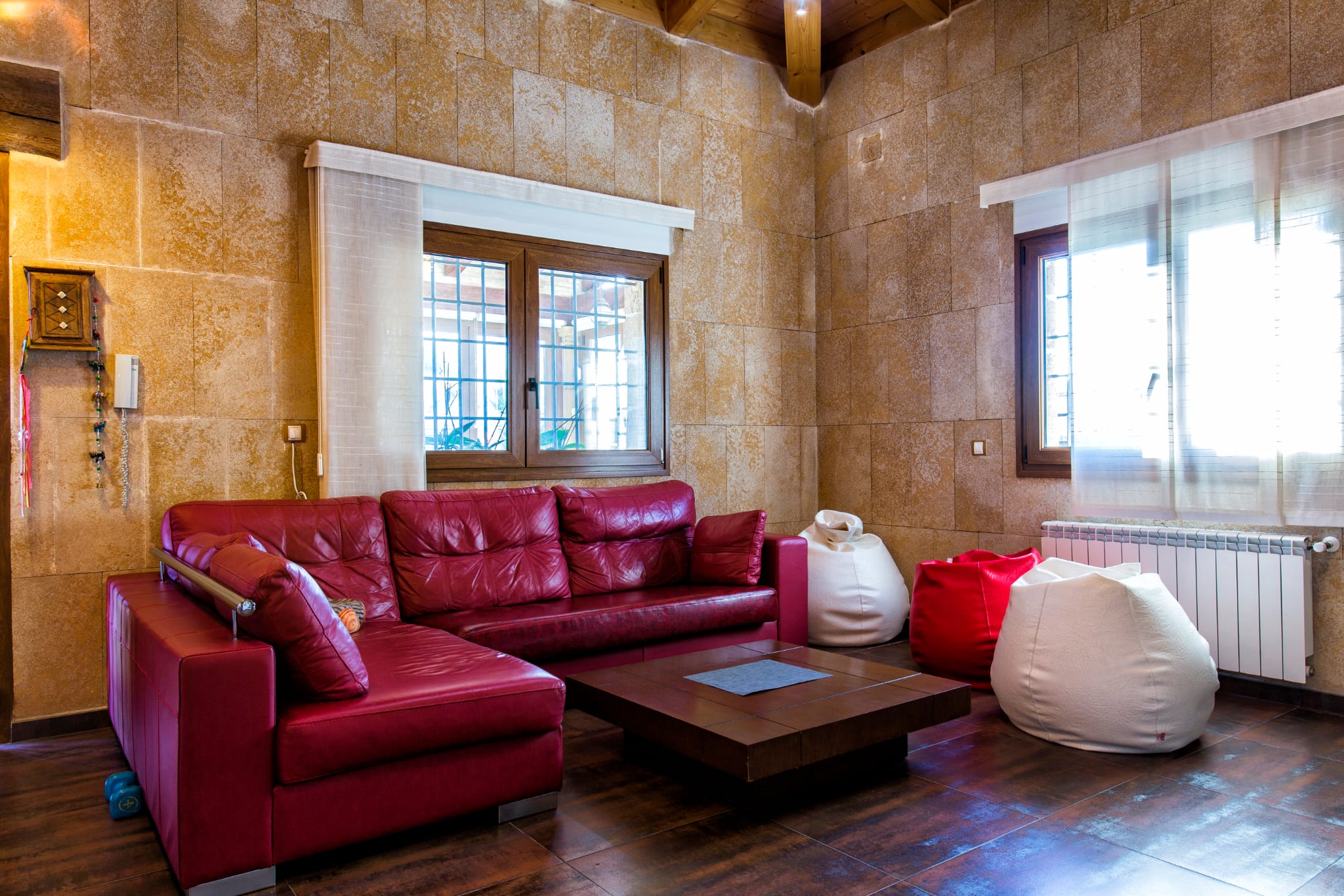 Living area featuring a red leather sectional sofa, stone-clad walls, and exposed wooden ceiling beams. Includes a low coffee table and bean bag seating.