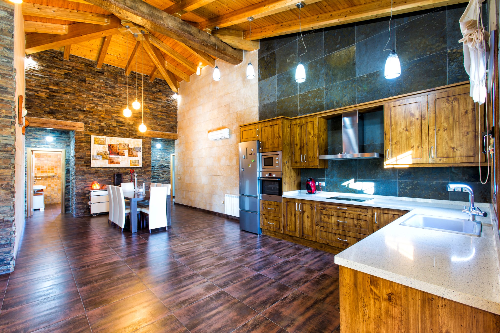 Open-plan kitchen and dining area featuring vaulted wooden ceilings, slate stone walls, rustic wood cabinetry, and integrated stainless steel appliances.