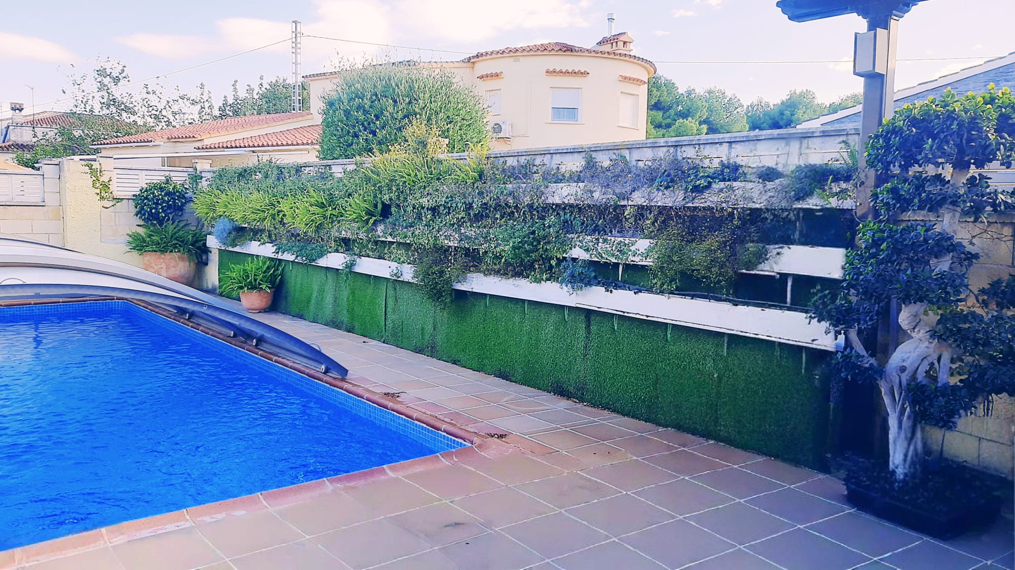 Outdoor swimming pool area featuring a tiled terrace, a retractable pool cover, and a tiered vertical garden wall with integrated artificial turf.