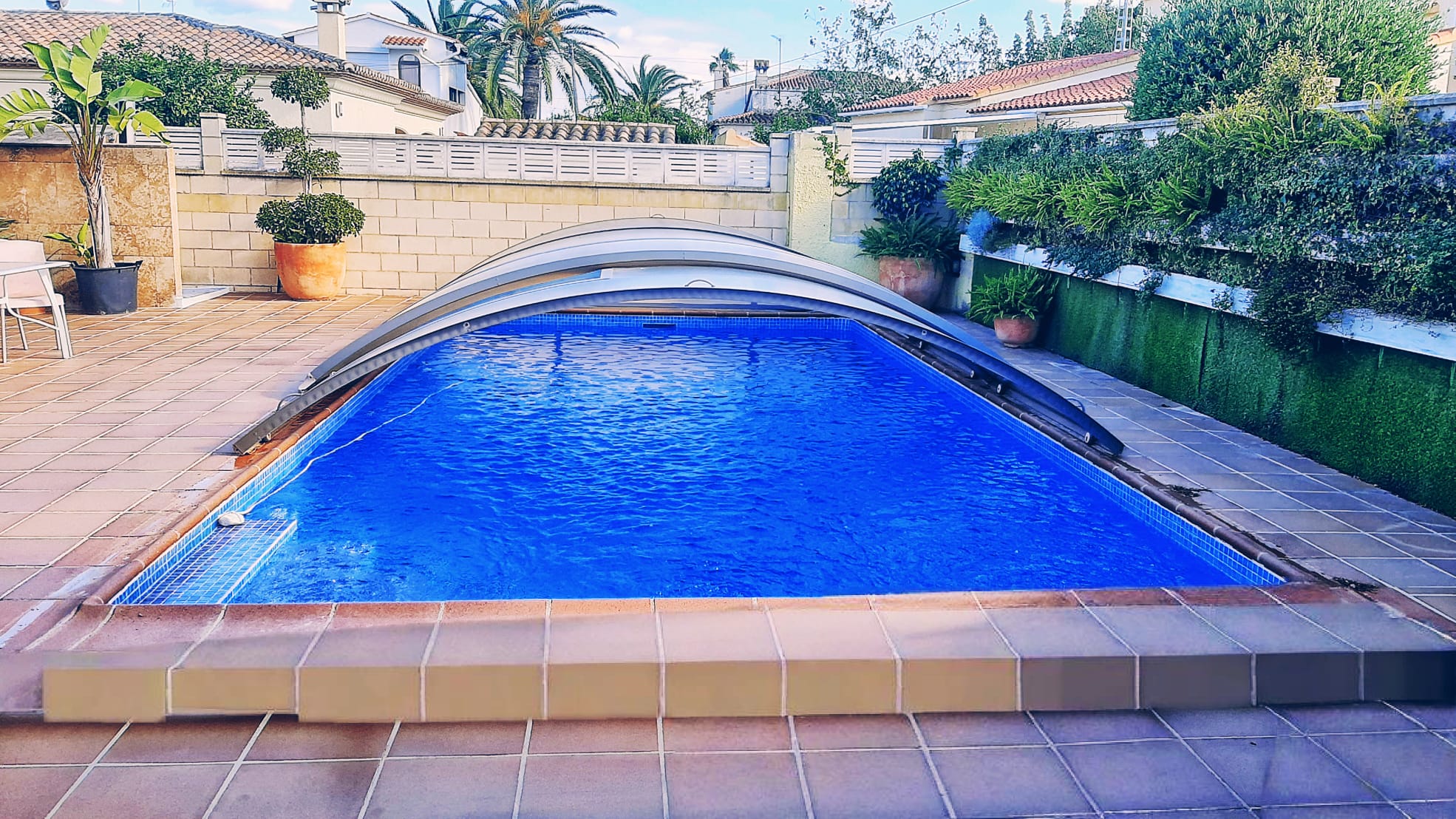 Private swimming pool featuring a retractable telescopic enclosure, set within a tiled terrace bordered by lush greenery and Mediterranean flora.