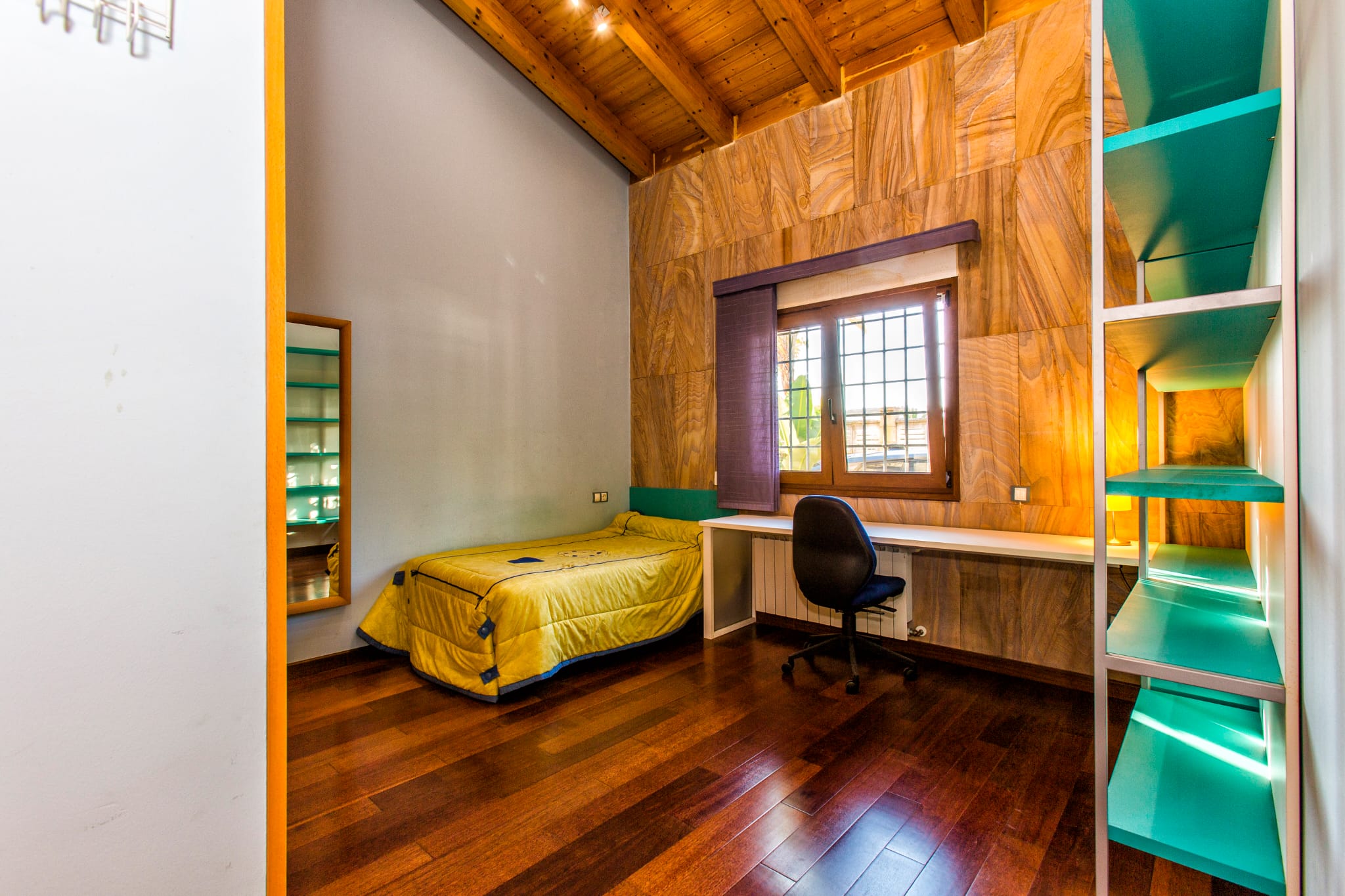 Single bedroom featuring vaulted wooden ceilings, a textured stone-effect feature wall, integrated workspace with a long desk, and dark hardwood flooring.