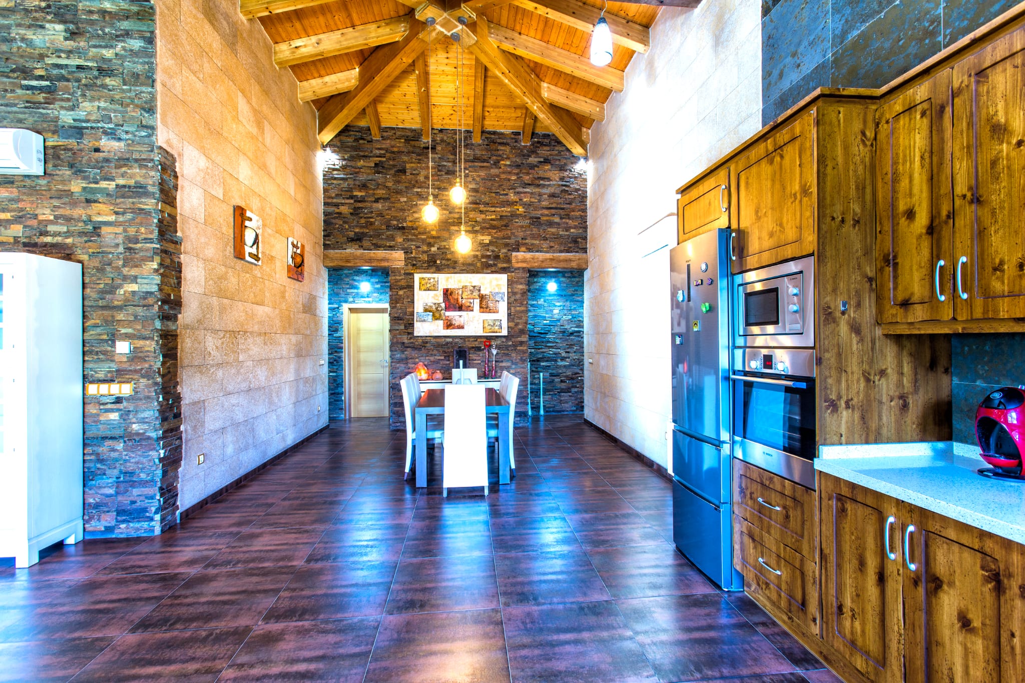 Spacious dining and kitchen area with vaulted wooden ceilings, stacked stone walls, and integrated stainless steel appliances.