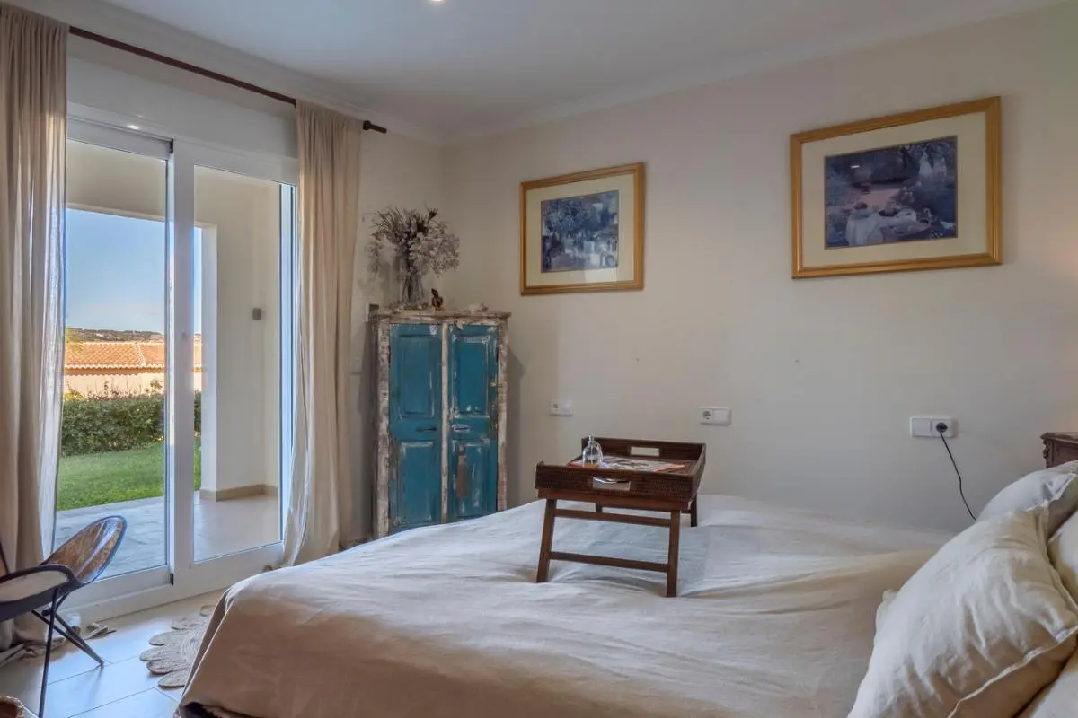 Bedroom featuring direct terrace access through sliding glass doors, a rustic blue wooden cabinet, and neutral-toned bedding with a wooden breakfast tray.