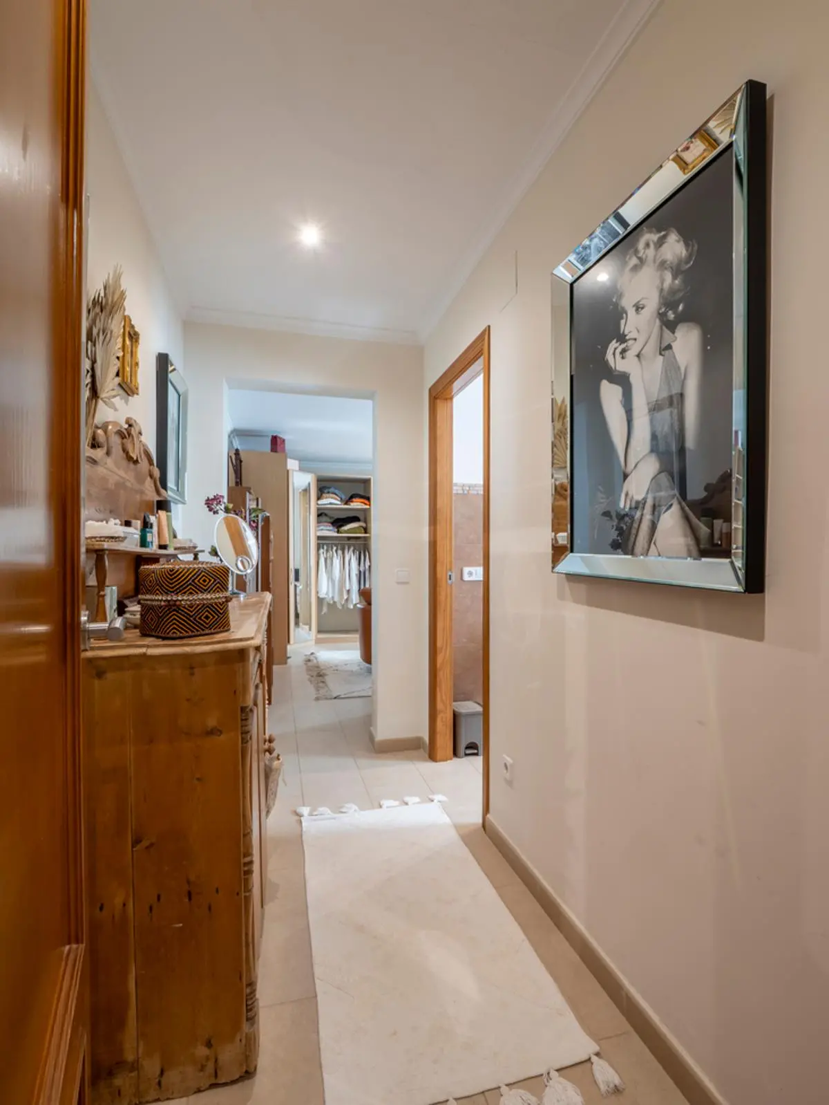 Bright hallway featuring a rustic wooden dresser, a large framed portrait with a mirrored border, and a direct view into an organized walk-in closet.