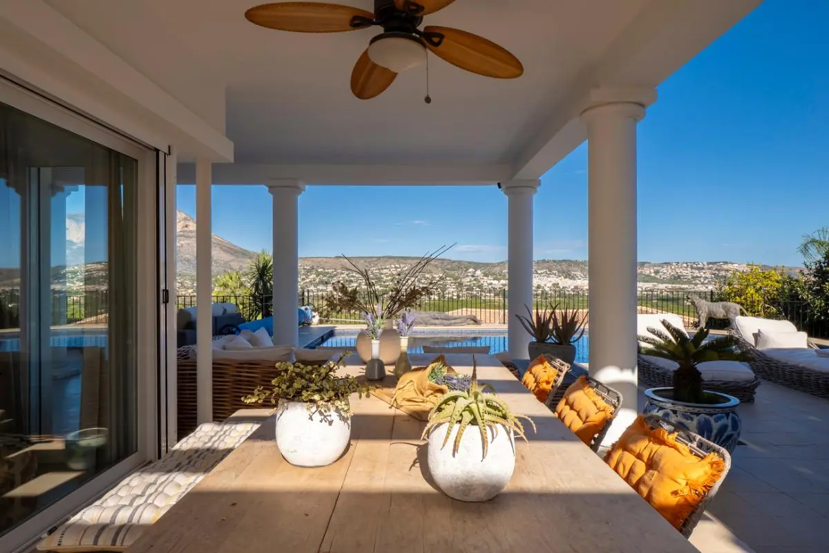 Covered terrace featuring a wooden dining table, natural wood ceiling fan, and panoramic views over the swimming pool and mountains.